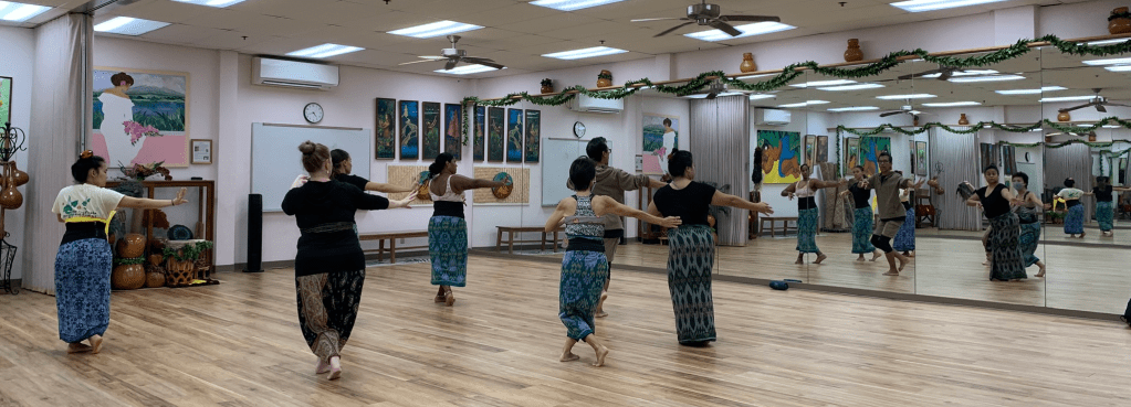 Five female dancers and two teachers perform in front of a mirror wall.