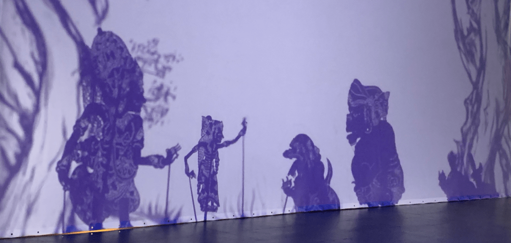 Four wayang listrik shadow figures on a projection screen.